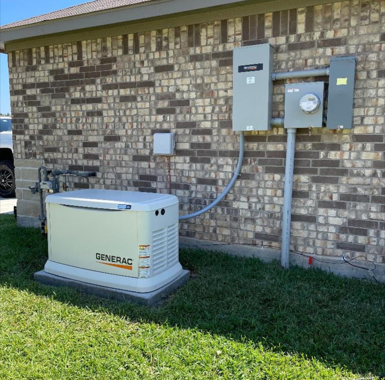 A standby generator on a pad beside a brick house, below the meter and transfer switch