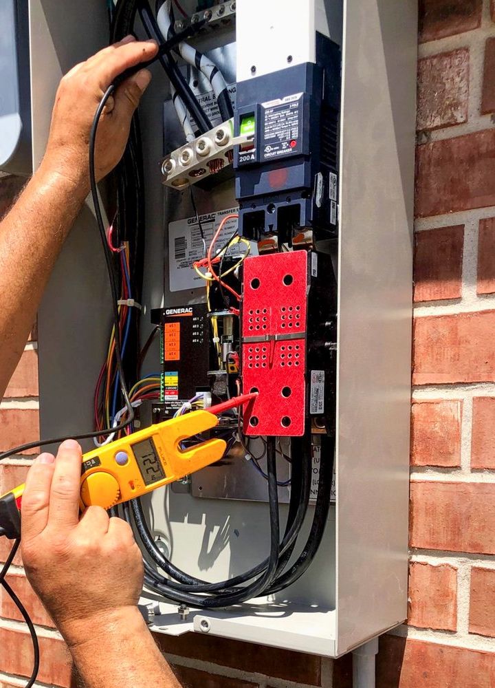 An electrician’s hands testing wiring inside an exterior panel with a clamp meter