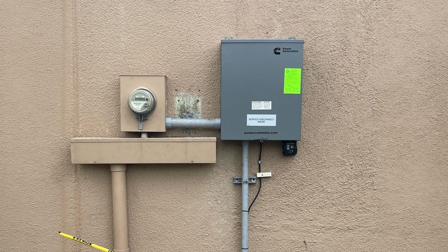 An electric meter and a transfer switch mounted on a stucco wall