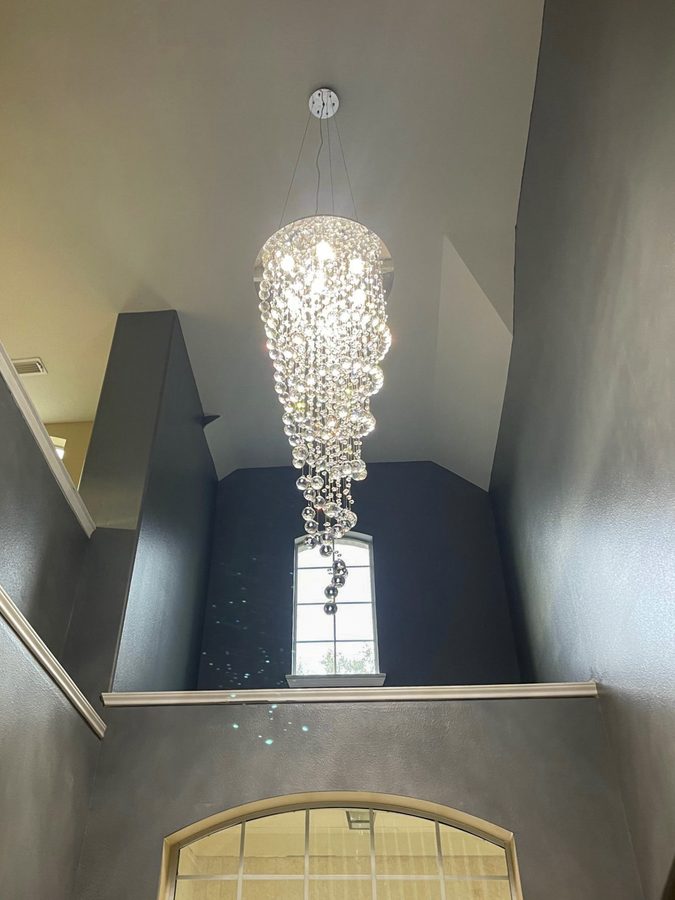 A tall crystal chandelier hanging in a narrow two-story entry