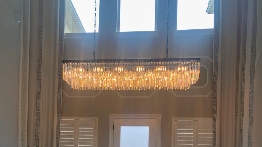A long linear crystal chandelier hung beneath a high window wall